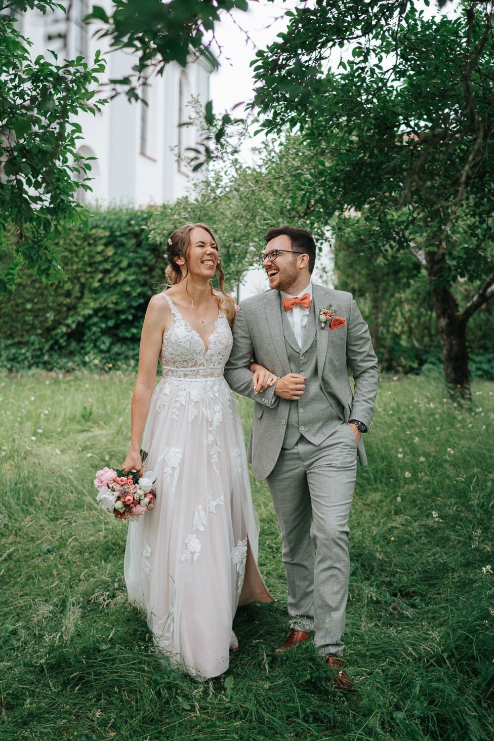 A couple shares a joyful moment walking together through a lush green apple orchard, captured in romantic wedding photos.