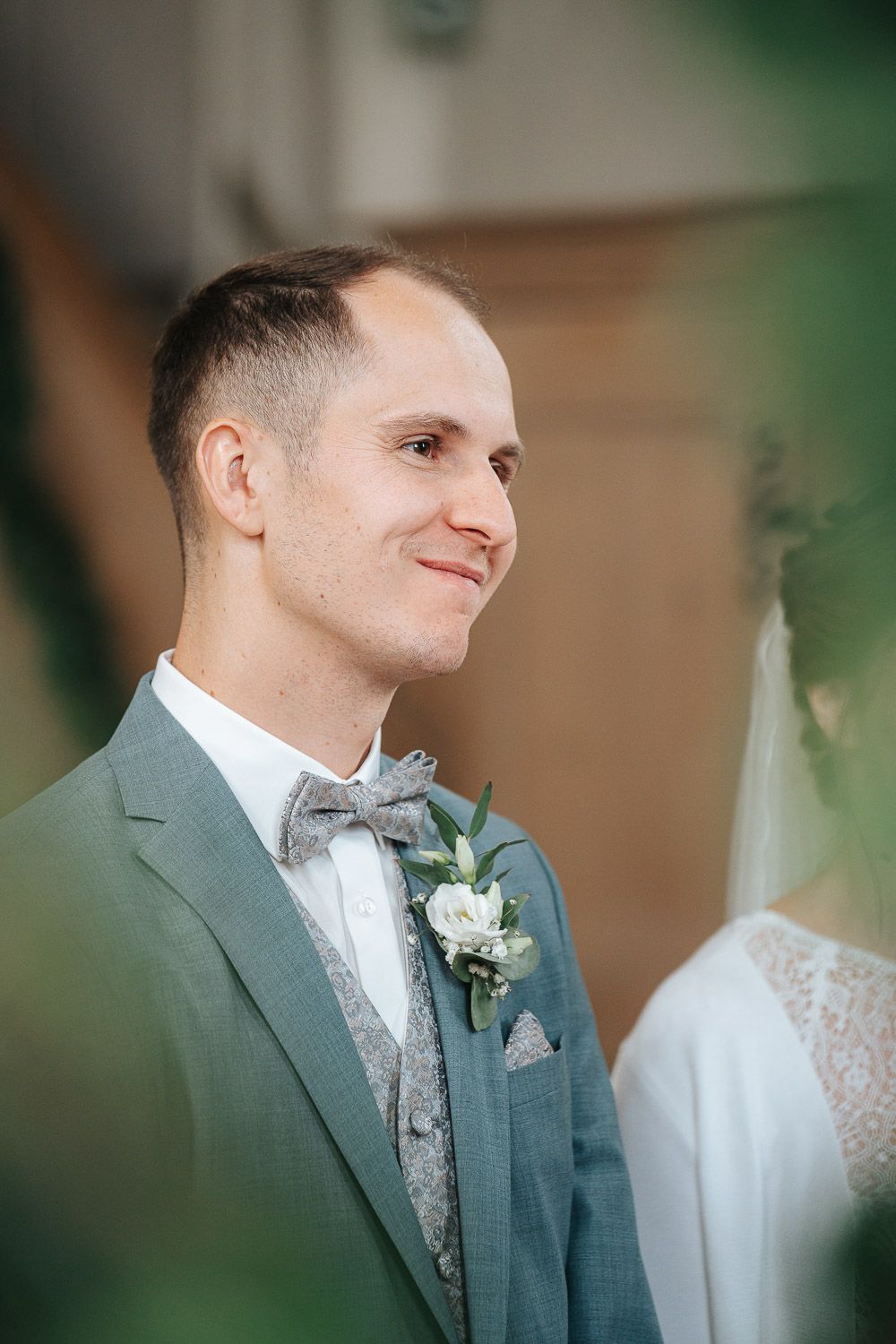 Side profile of someone on their wedding day wearing a gray suit and silver bowtie with boutonniere, looking off camera.