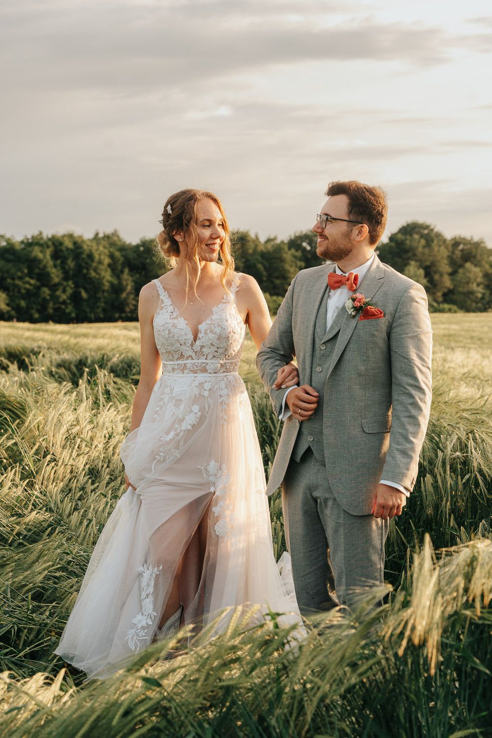 Romantic wedding couple in formal attire share joyful moments together in a golden wheat field at sunset.