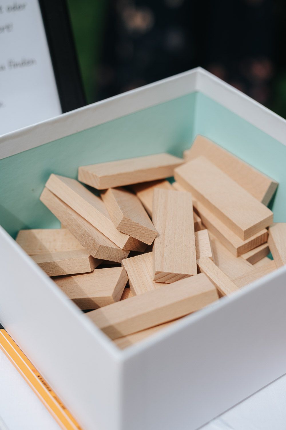 Wooden domino or tile pieces scattered inside a white rectangular container on a light blue surface.
