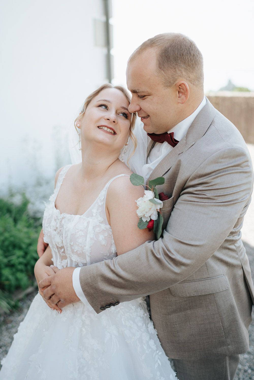 Romantic wedding scene with couple embracing in gray suit and white gown outdoors.