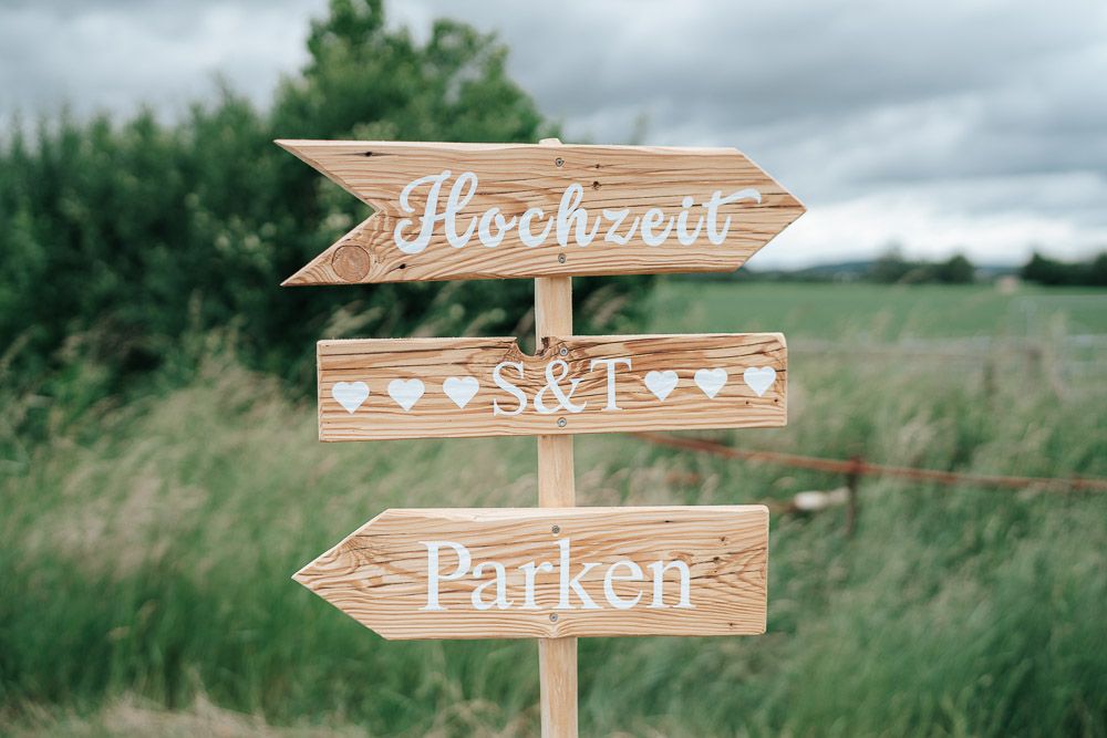 A wooden directional sign with German text 'Hochzeit' and 'Parken' displays wedding directions in a rustic outdoor setting.