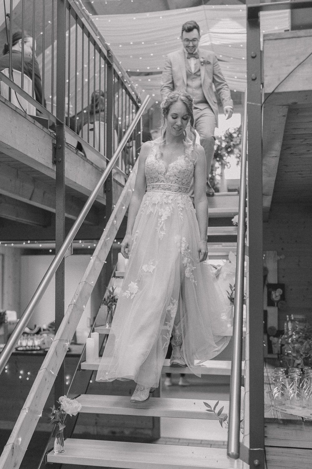 Classic black and white photo of a wedding couple descending a staircase in formal wedding attire.