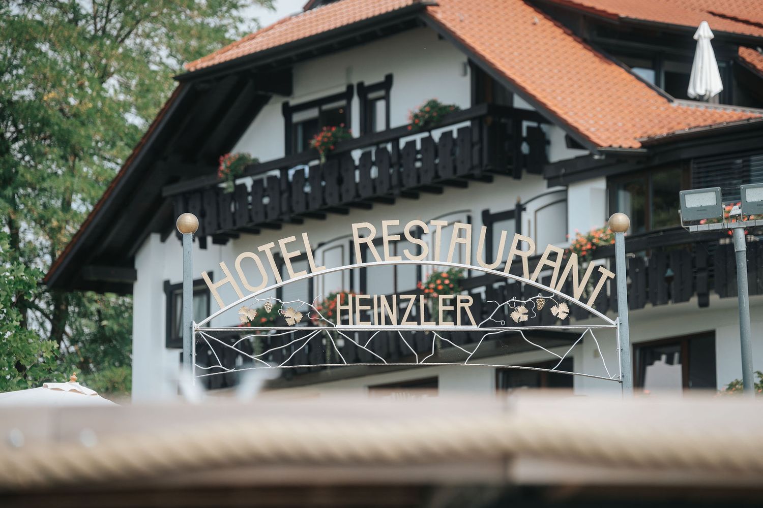 Hotel Restaurant Heinzler sign on a white alpine-style building with wooden balconies and a red tile roof, surrounded by green trees.