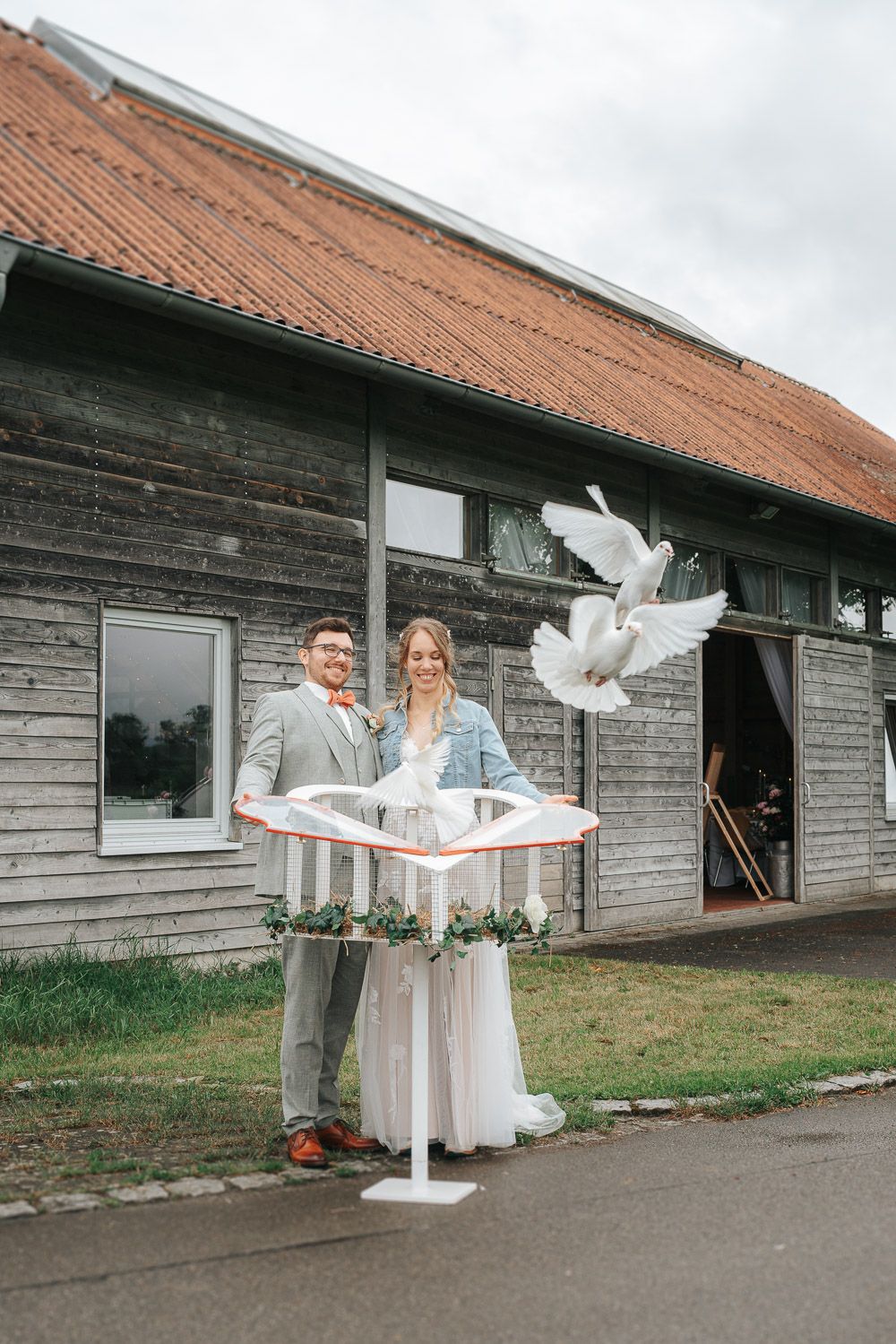 A couple releases white doves from a cage during their outdoor barn wedding celebration.