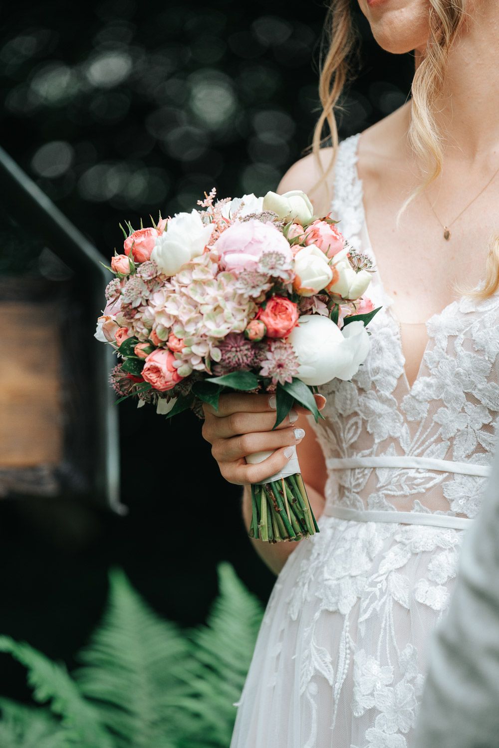 Close-up view of a delicate white lace wedding dress bodice with a romantic blush and cream floral bouquet.