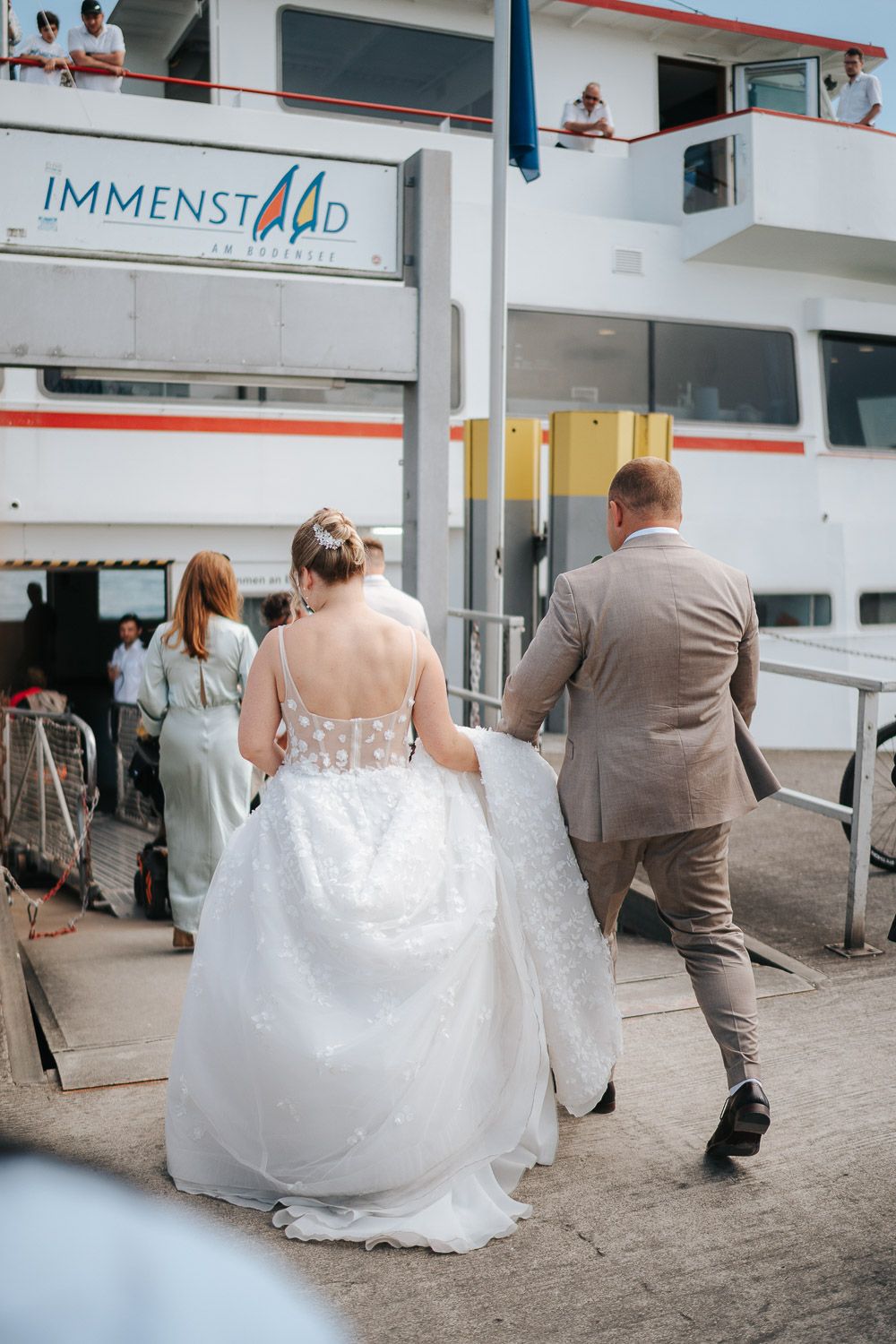 Wedding couple boarding the Immenstad cruise ship with bride wearing flowing white gown and groom in tan suit.
