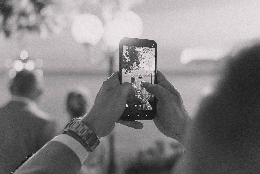 Someone holds up a smartphone to capture a moment at what appears to be a concert or event in black and white.