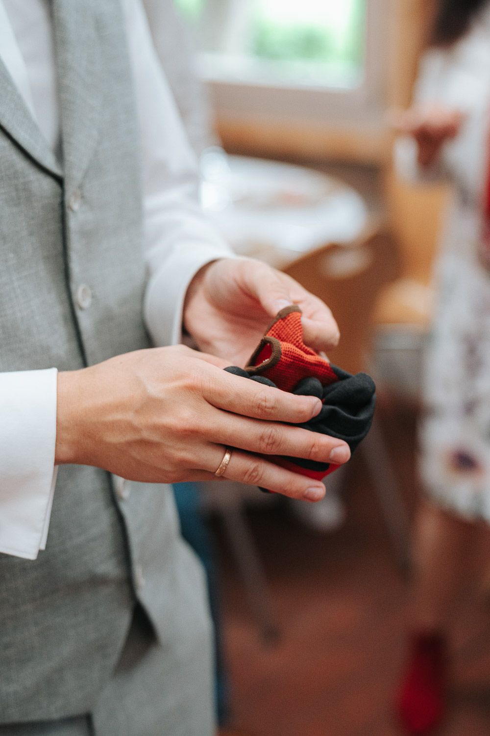 Close-up view of hands holding red and black rings against a grey suit and light background.