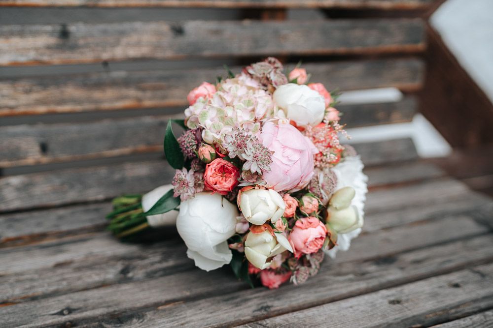 A pink and white floral bouquet sits on rustic wooden decking featuring roses and soft romantic blooms.