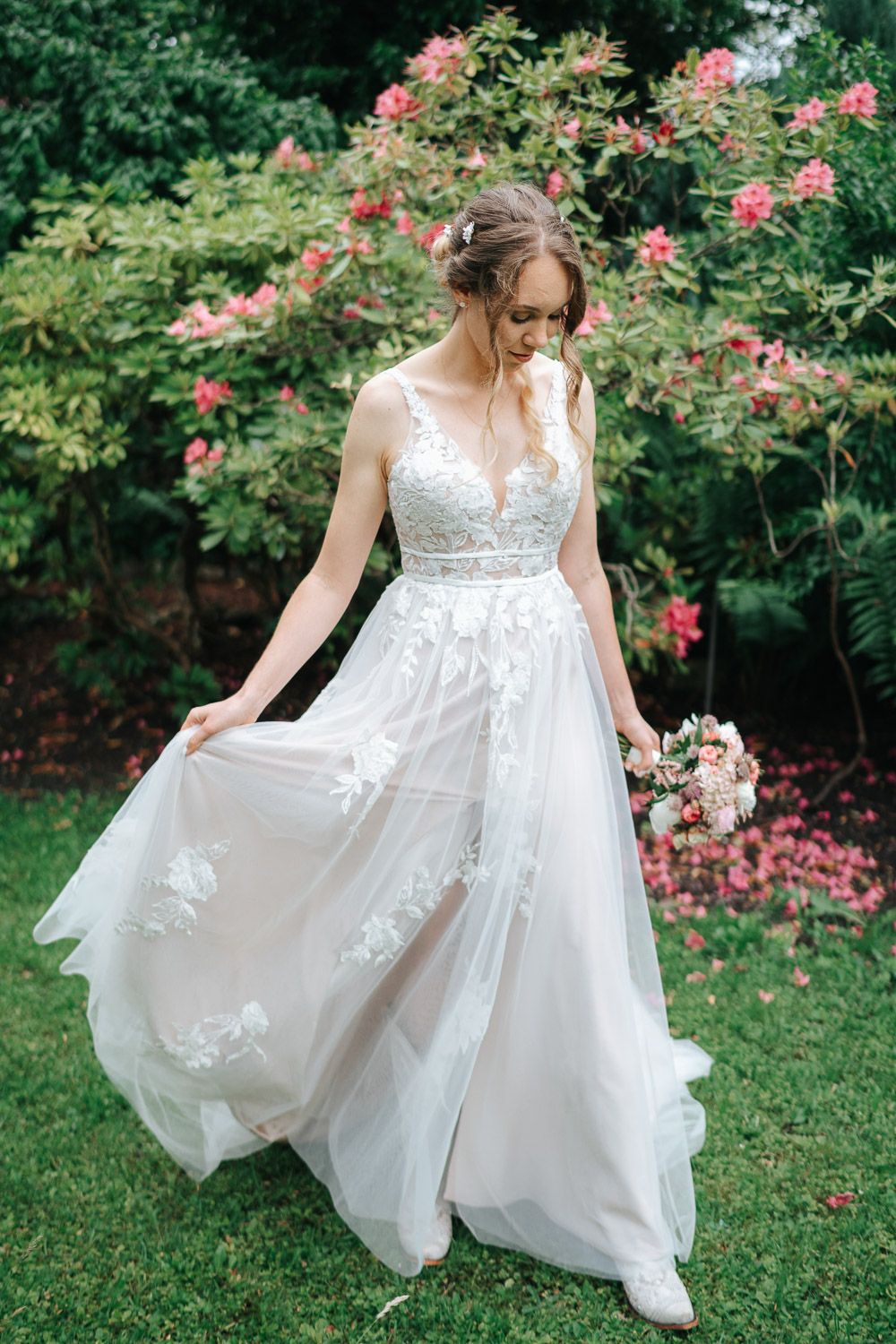Ethereal wedding gown with lace detail and flowing tulle skirt shown in garden setting with blooming roses.