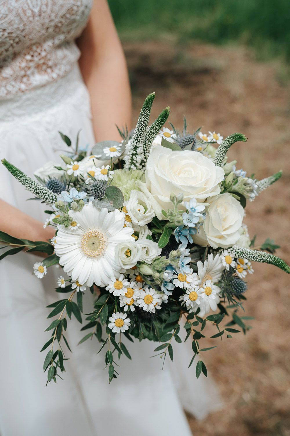 White and ivory bridal bouquet featuring roses, daisies, and eucalyptus greenery sits elegantly against a flowing dress.