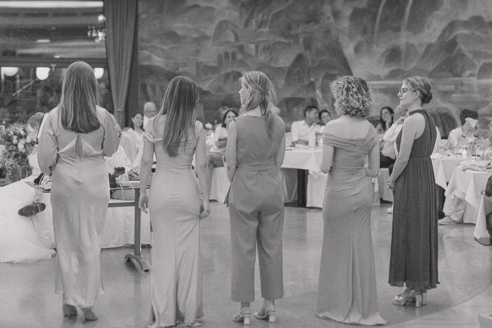 People dancing in a line formation at a party wearing casual and formal dresses in a black and white photograph.