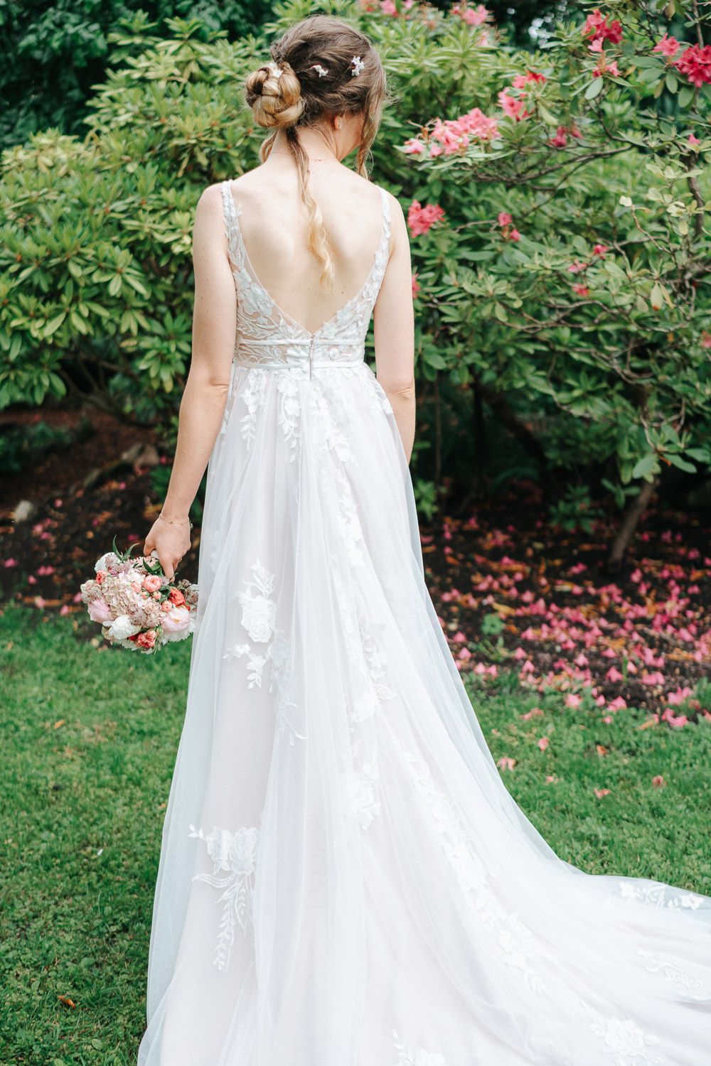 Back view of flowing white wedding dress with lace details and sweeping train in a garden setting.