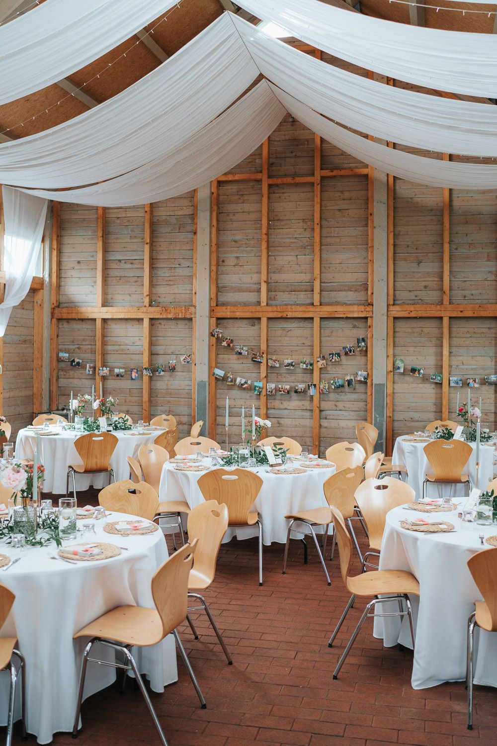 Rustic barn venue with white drapes and round tables decorated for an elegant wedding reception with twinkling string lights.