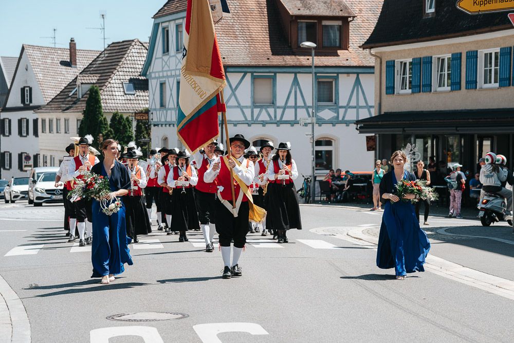 A traditional German cultural parade marches through a town street with people in traditional Bavarian folk costumes and flags.