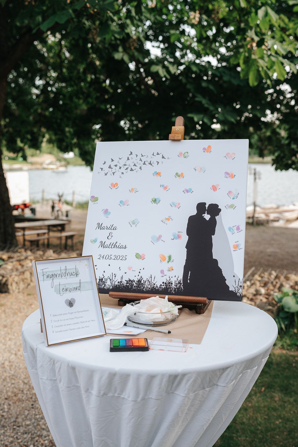 A wedding guest book table with a silhouette art piece, white tablecloth, and colorful ink pads for fingerprint signing.