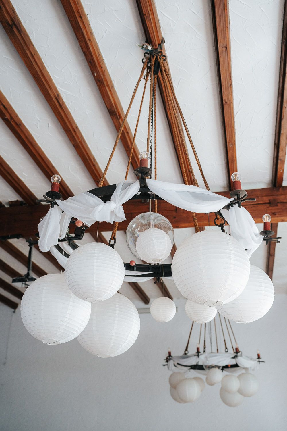 White paper lanterns hang decoratively from exposed wooden ceiling beams in an airy interior space.