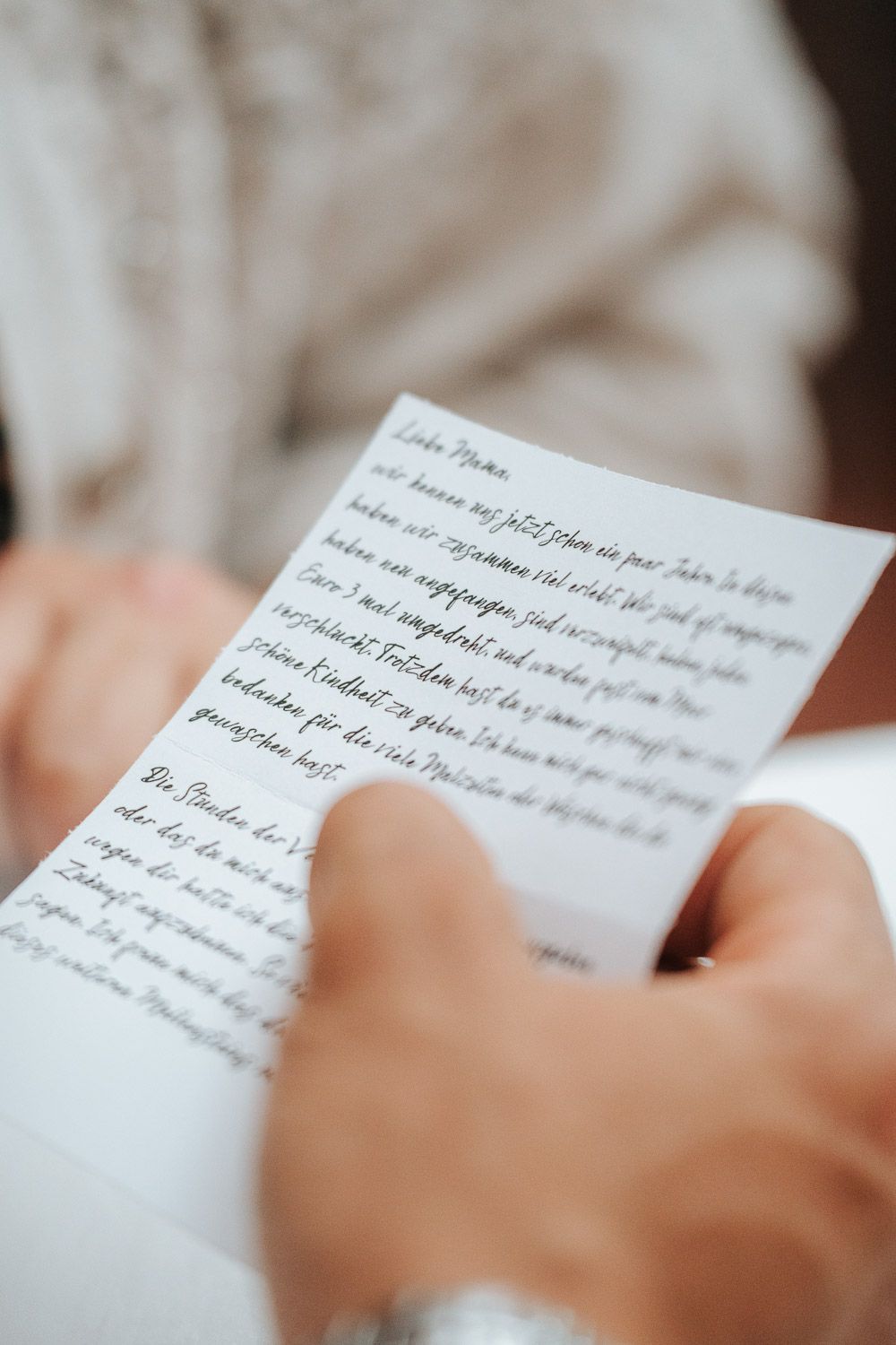Hands holding a handwritten letter on white paper, captured in soft focus with shallow depth of field.