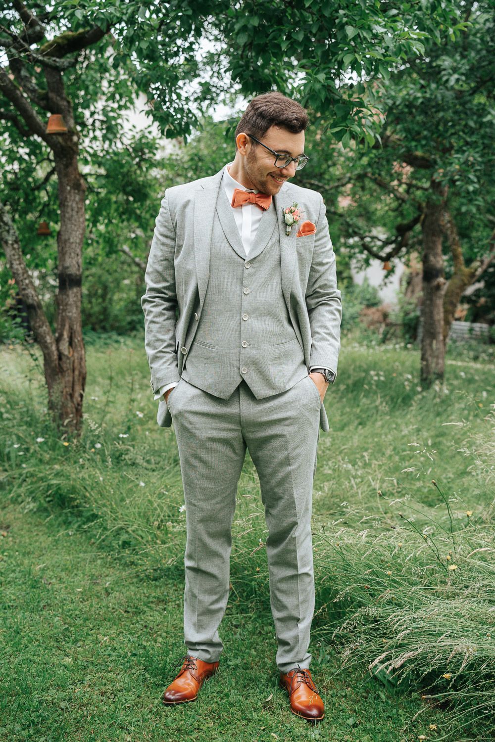 Wedding attire featuring a light gray suit with orange accents in an outdoor garden setting.