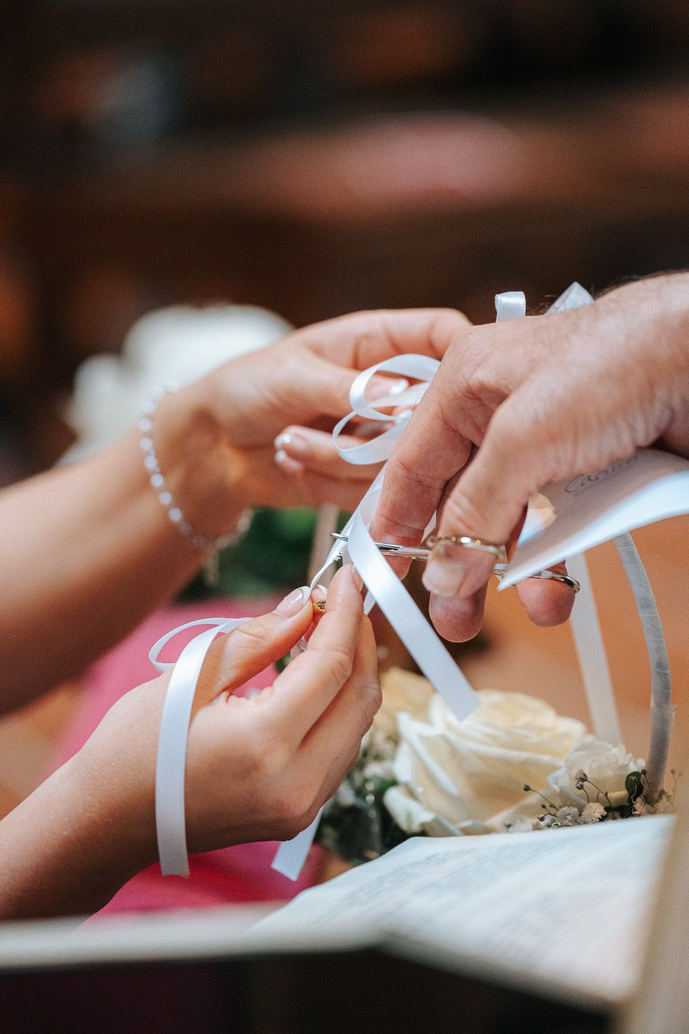 Hands passing along a white ribbon in a continuous line during a group activity or ceremony.