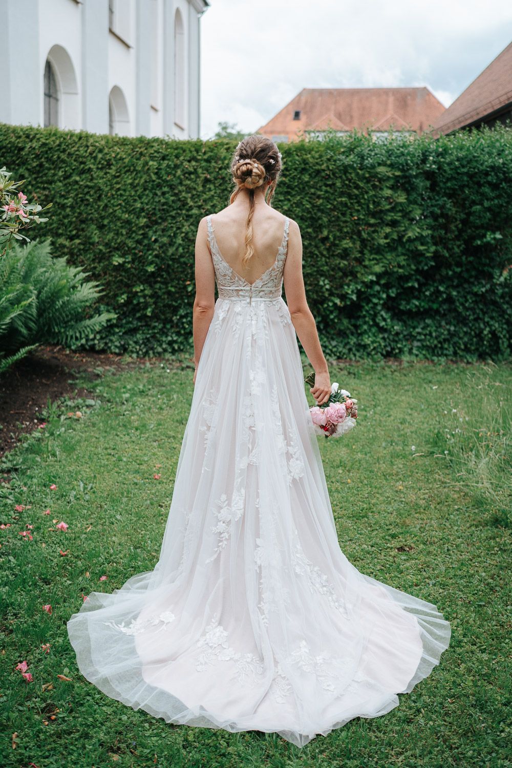 Elegant white wedding dress with lace details and long train photographed from behind in a garden setting.