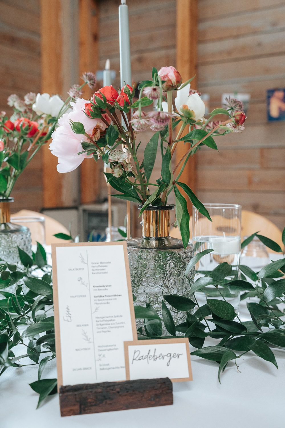 Elegant wedding reception table decor with floral centerpiece, menu card and greenery on white tablecloth in rustic venue.
