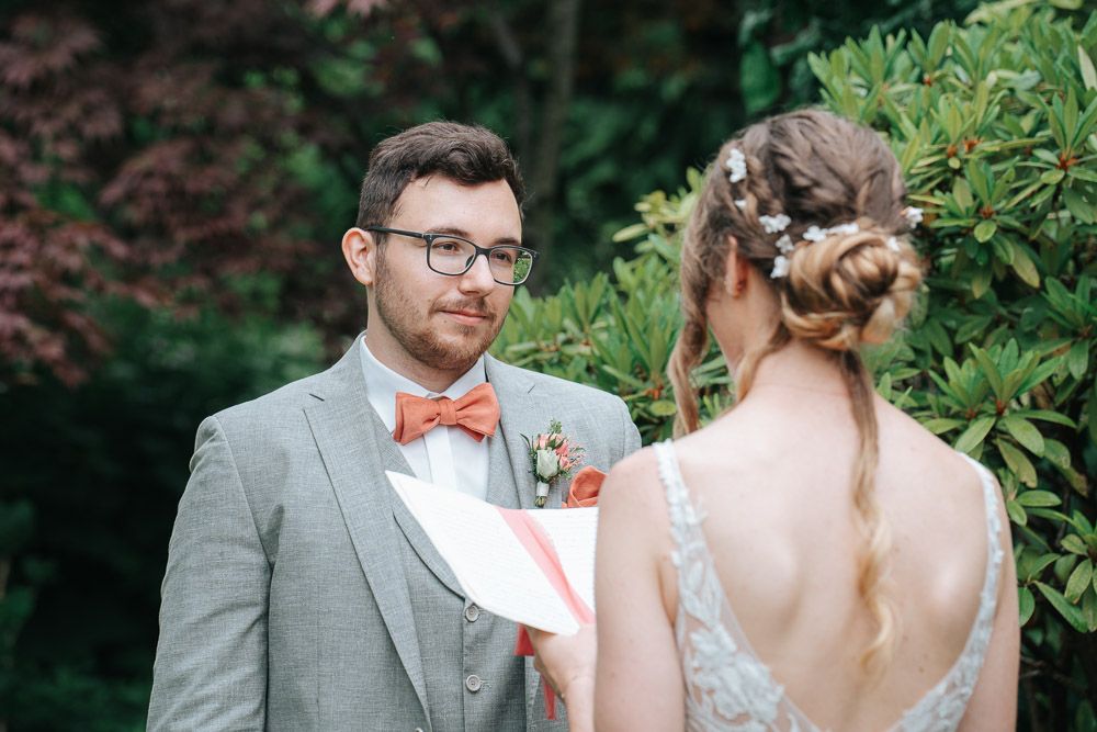 Wedding couple shares intimate moments in a lush garden setting wearing elegant gray and peach attire.