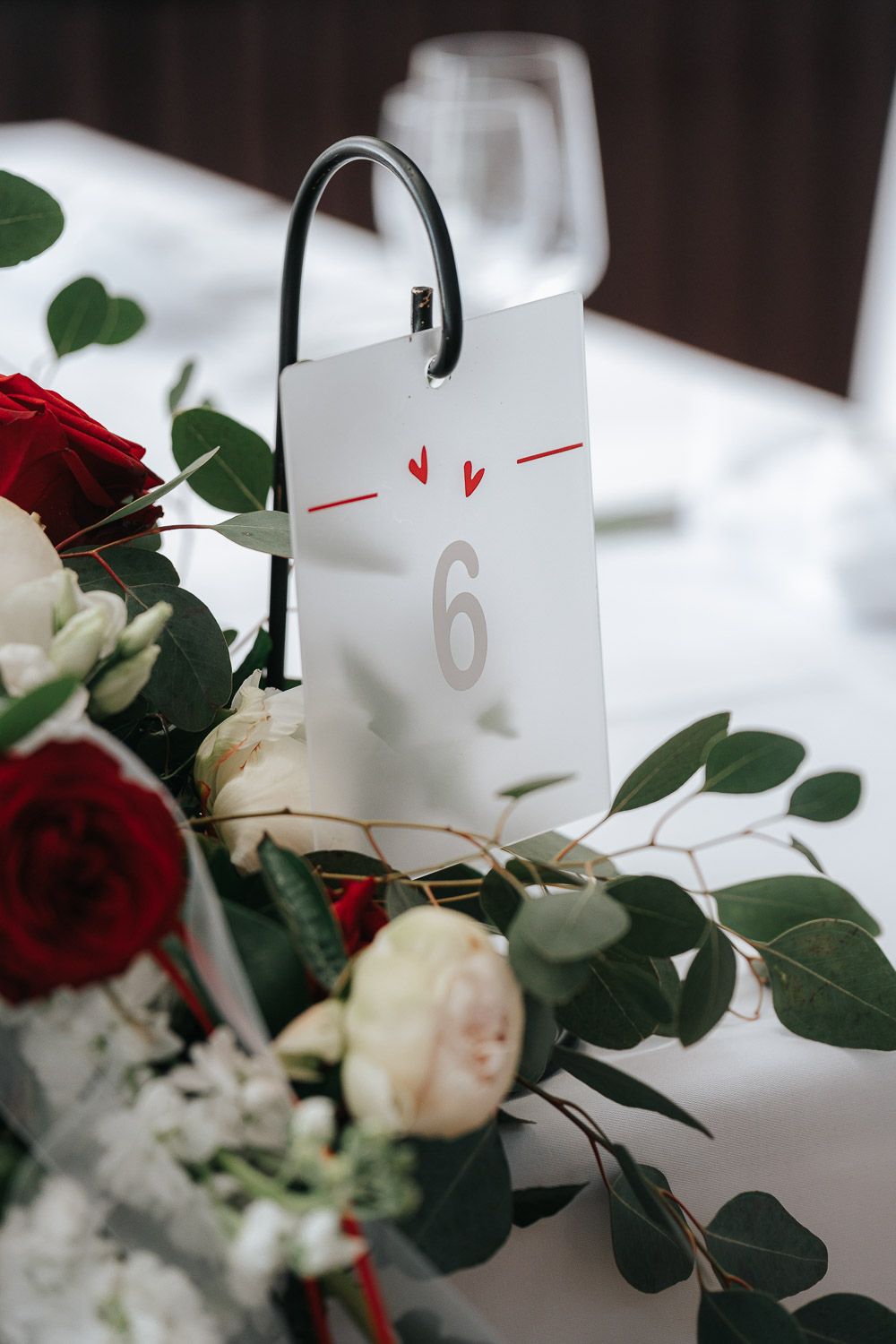 Wedding table centerpiece with red and white roses alongside table number 6 card on crisp white tablecloth.