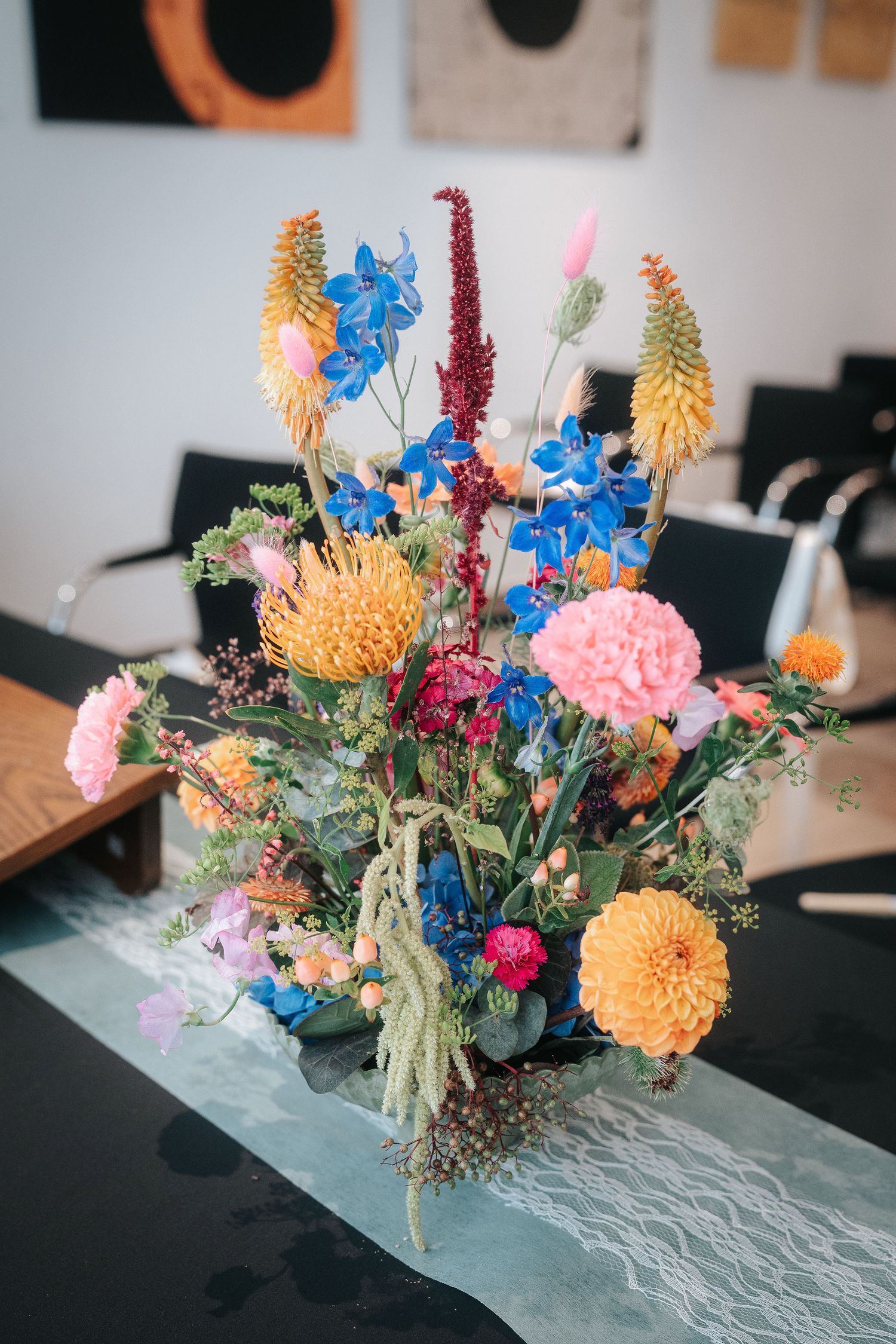 Colorful wildflower bouquet with blue delphinium, orange dahlias, pink blooms and red amaranthus on a table with a lace runner.