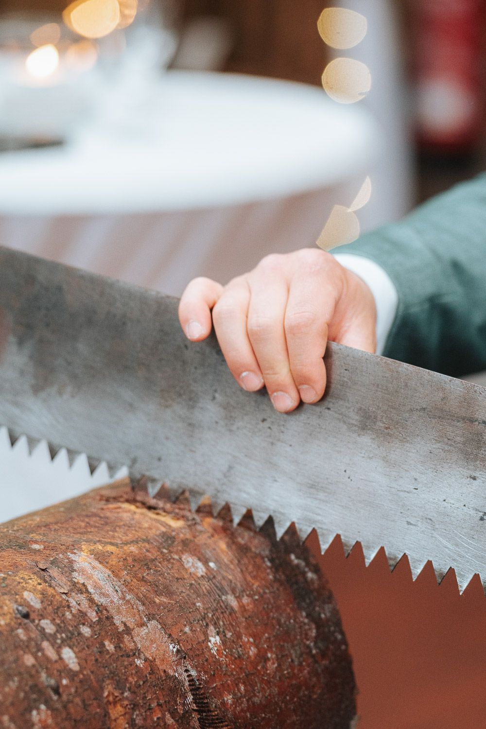 A close-up shot of hands using a large rustic saw blade on a piece of rough wood.