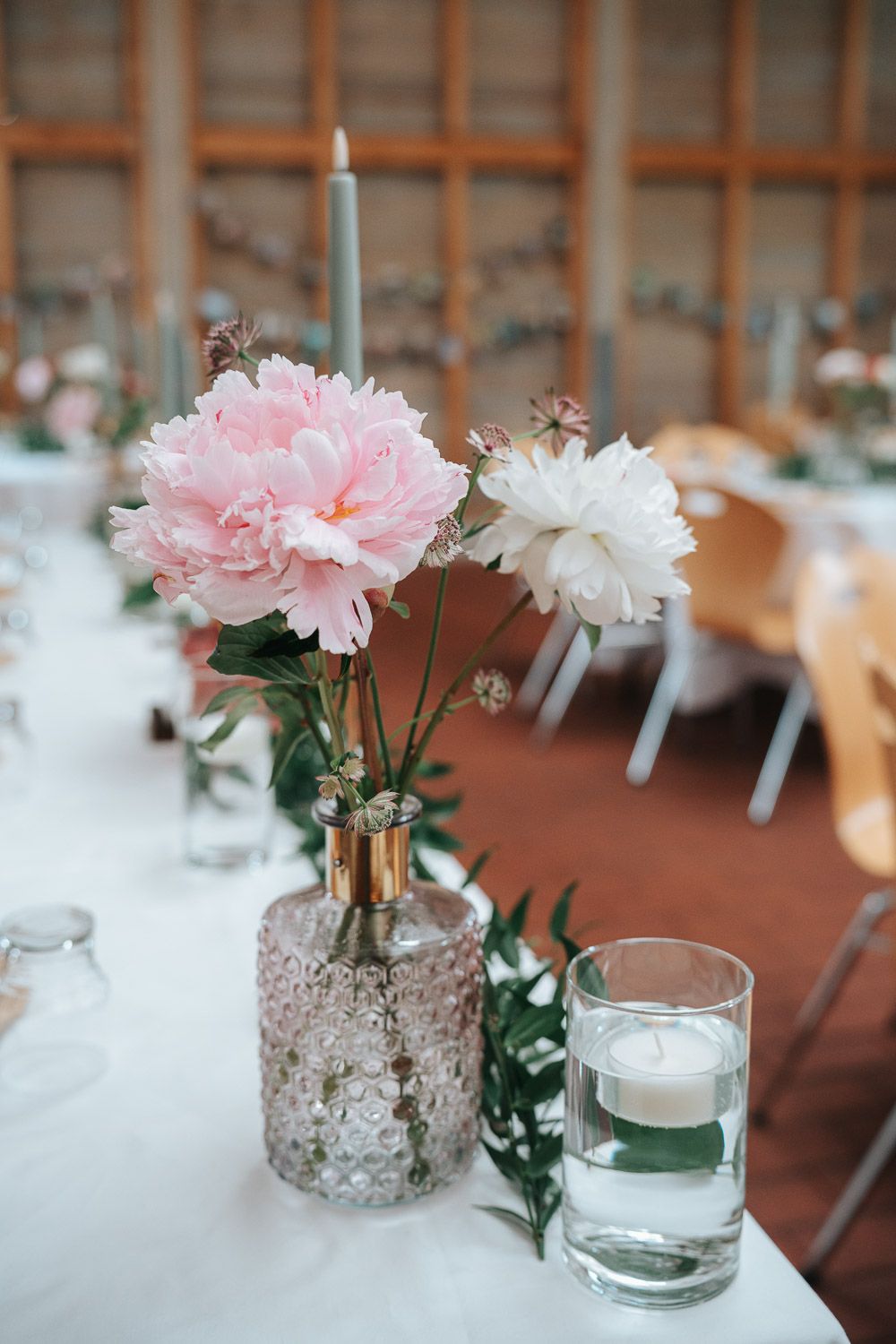 Pink and white carnations in delicate lace-wrapped vases with floating candles create an elegant table centerpiece.