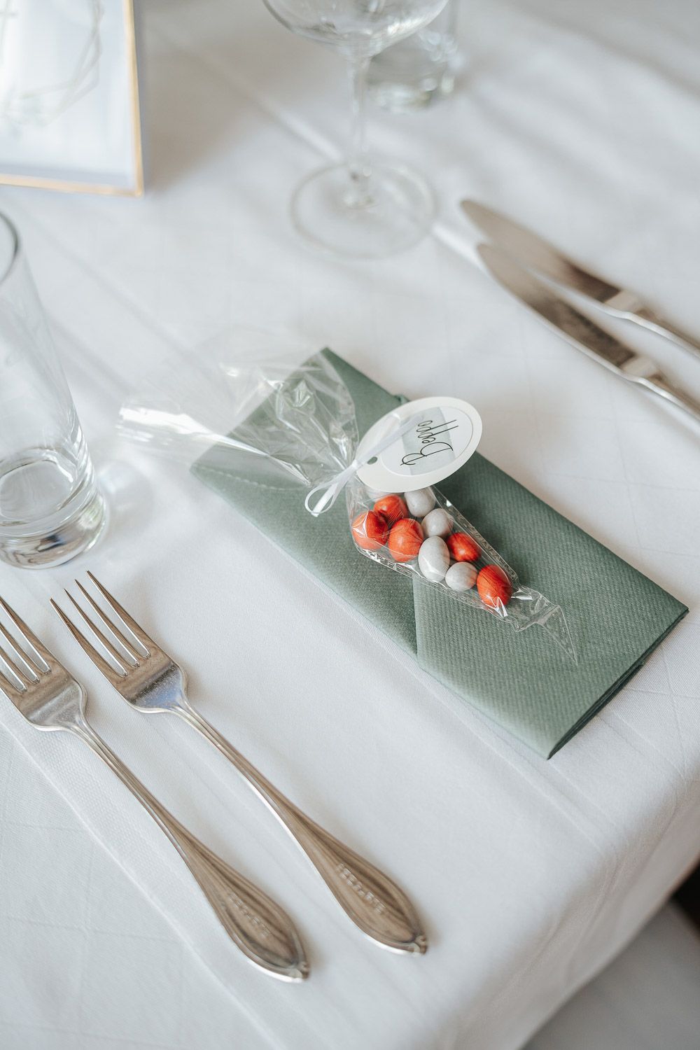 Table place setting with white napkins, sage green accent napkins, and small decorative red berries for elegant dining.