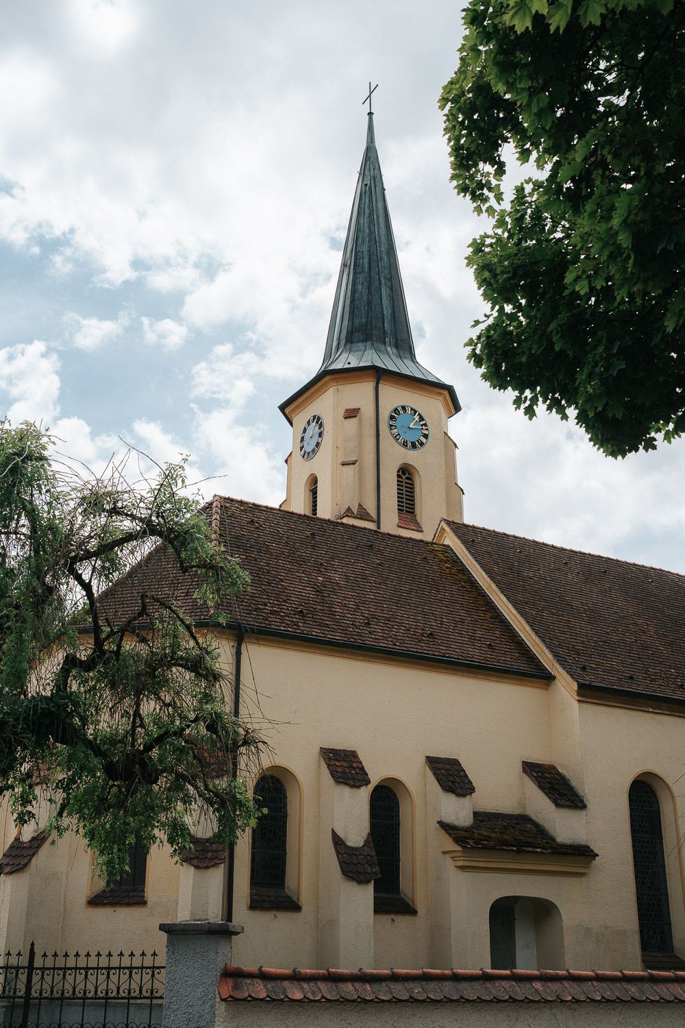 Historic church building with multiple spires and arched windows set against a cloudy sky and trees.