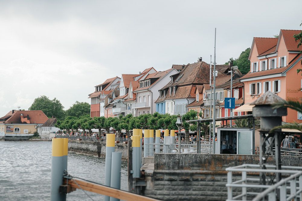Waterfront row houses with colorful facades line the harbor dock with mooring posts in Überlingen, Germany.