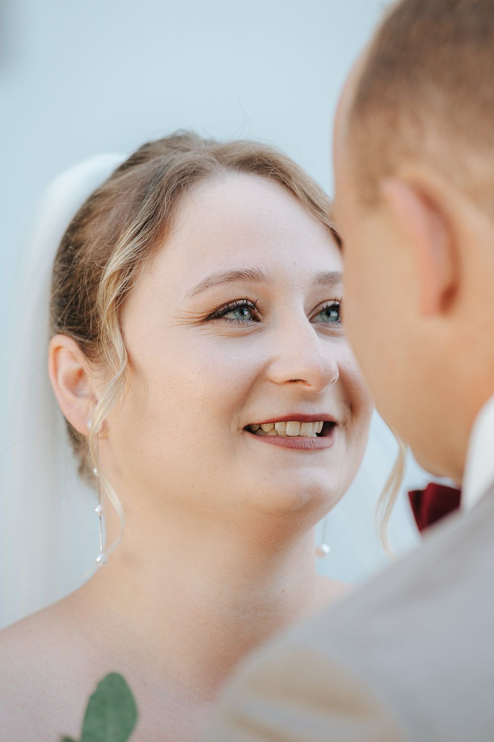 Close-up photo of a smiling bride in natural lighting, radiating joy during a wedding moment.