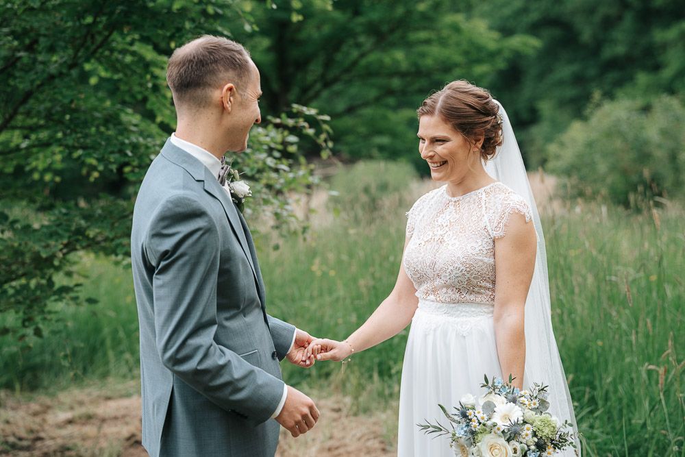 A couple in wedding attire exchanges rings during an intimate outdoor ceremony in a lush natural setting.