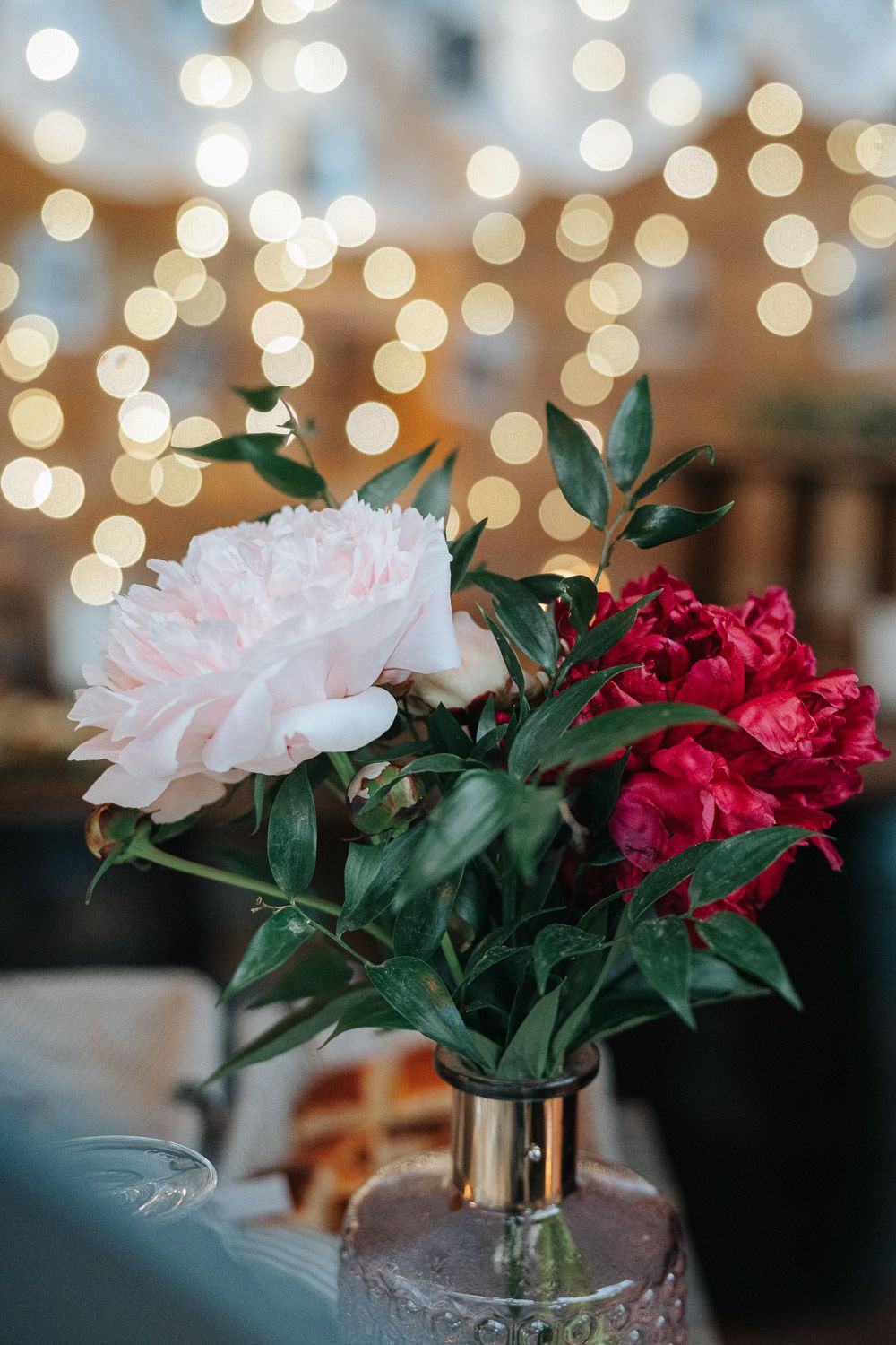 Pink and red carnations in glass vase with blurred bokeh lights in the background create an elegant display.