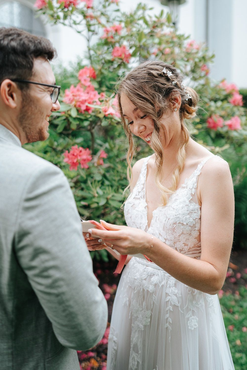 A couple exchanges rings during an intimate garden wedding ceremony with pink flowers blooming in the background.