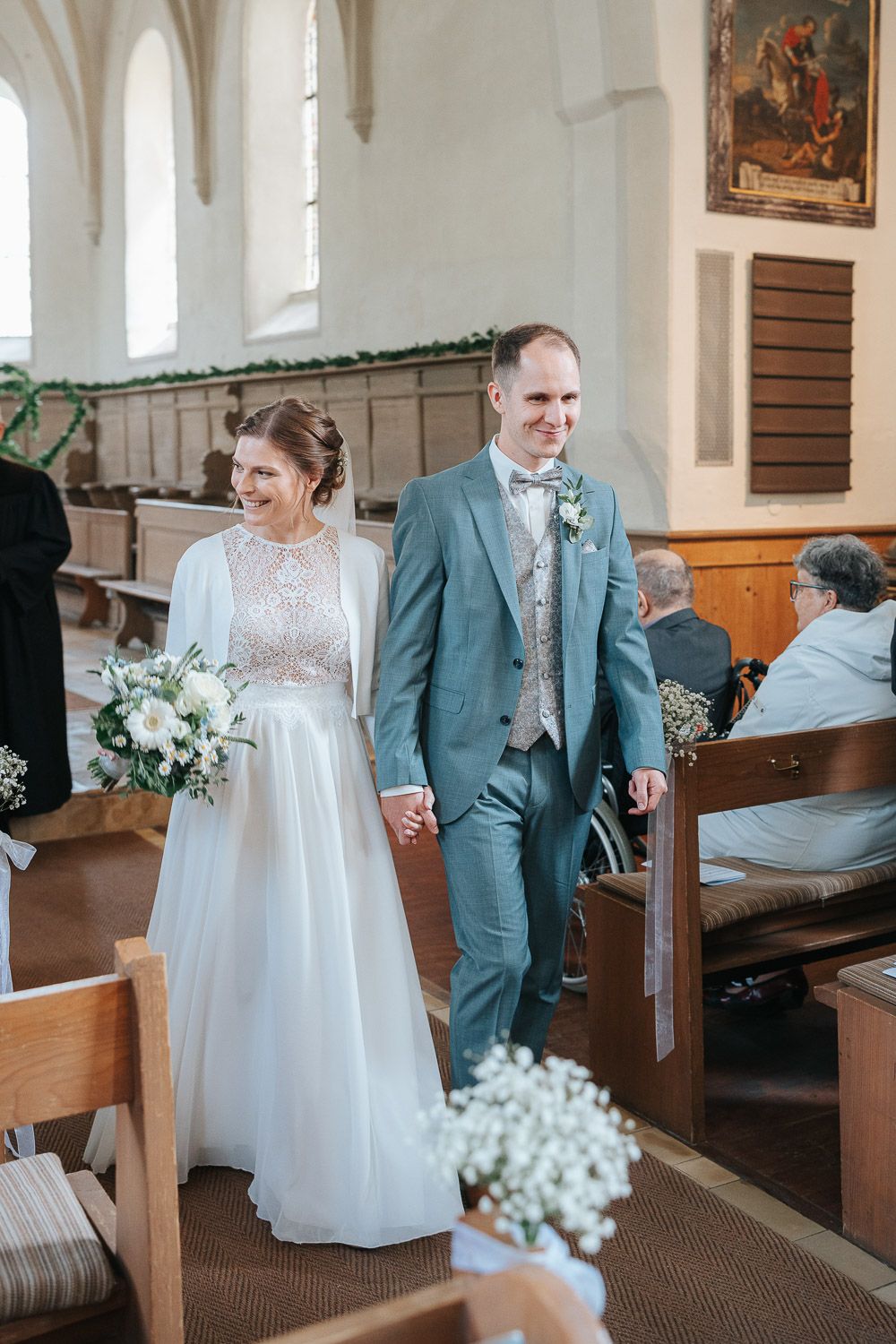 A romantic church wedding scene showing a couple in elegant wedding attire standing together in church pews.