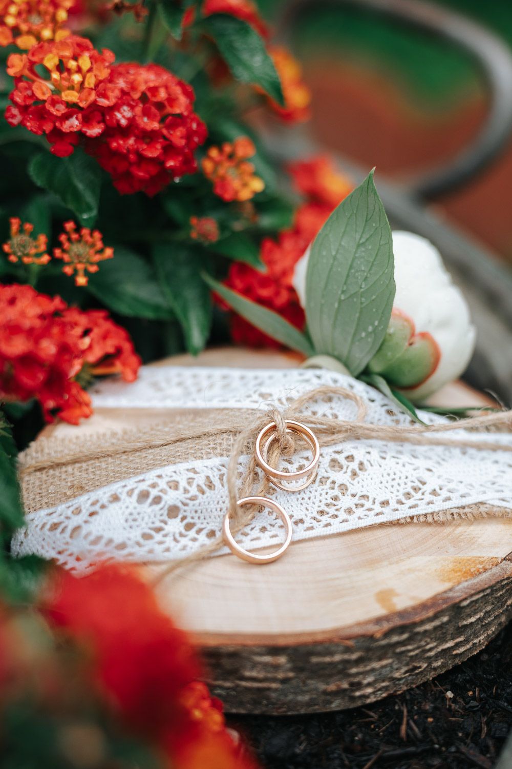 A rustic wooden surface decorated with lace ribbon and red lantana flowers creating an elegant decorative arrangement.