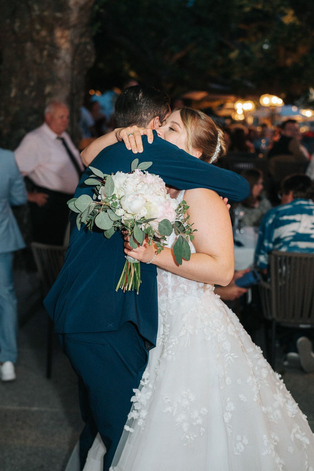 A newlywed couple shares their first dance at an outdoor evening wedding reception surrounded by romantic lighting.