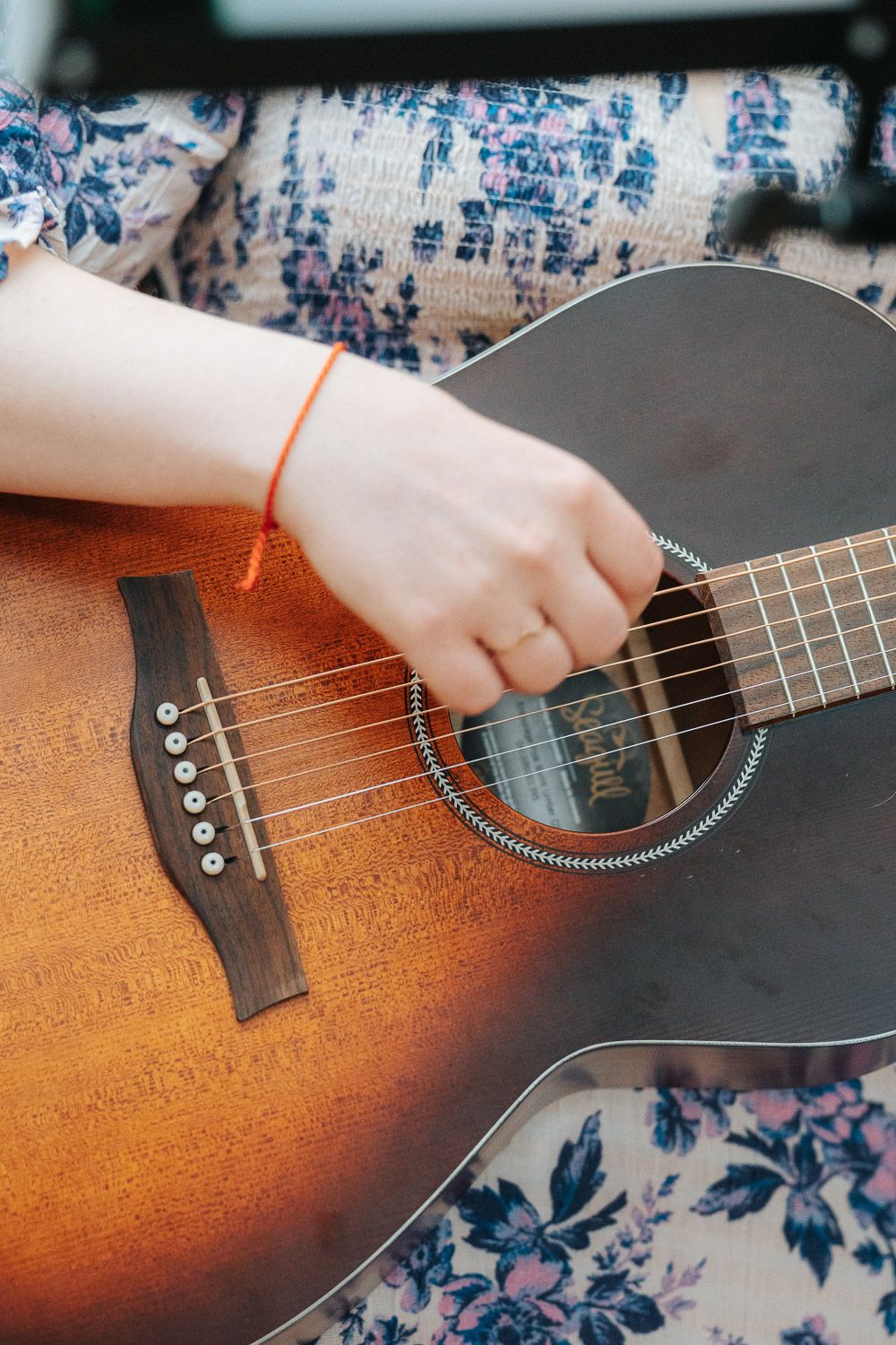Close-up view of brown sunburst acoustic guitar with strings being played against floral patterned background.