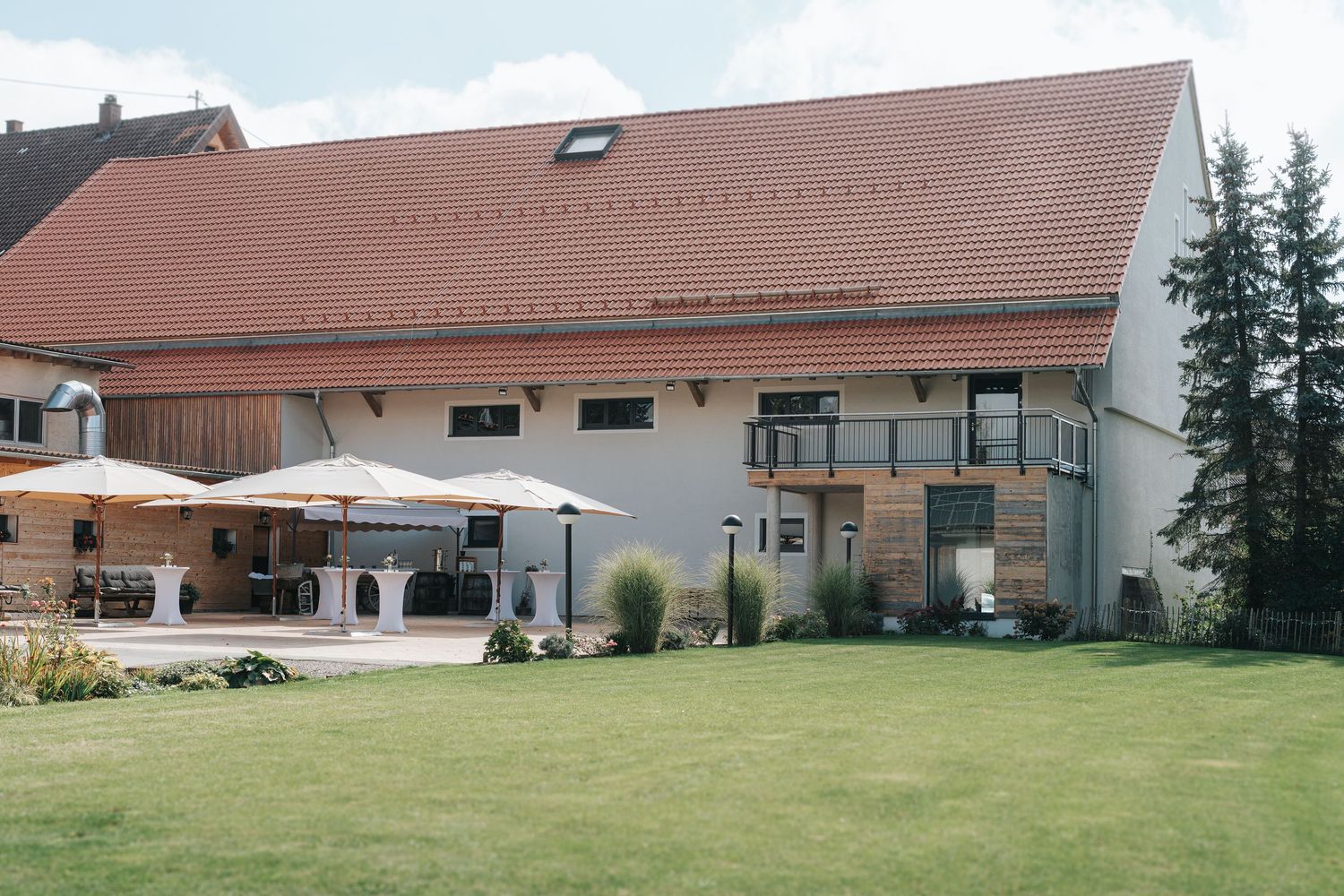 Modern white farmhouse with red tile roof sits on expansive green lawn surrounded by rural countryside.