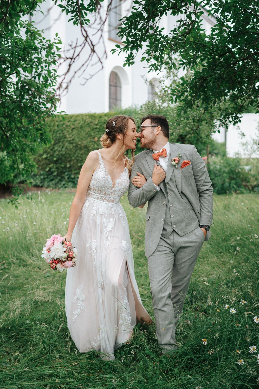 A couple in wedding attire shares intimate moments in a lush green garden setting.