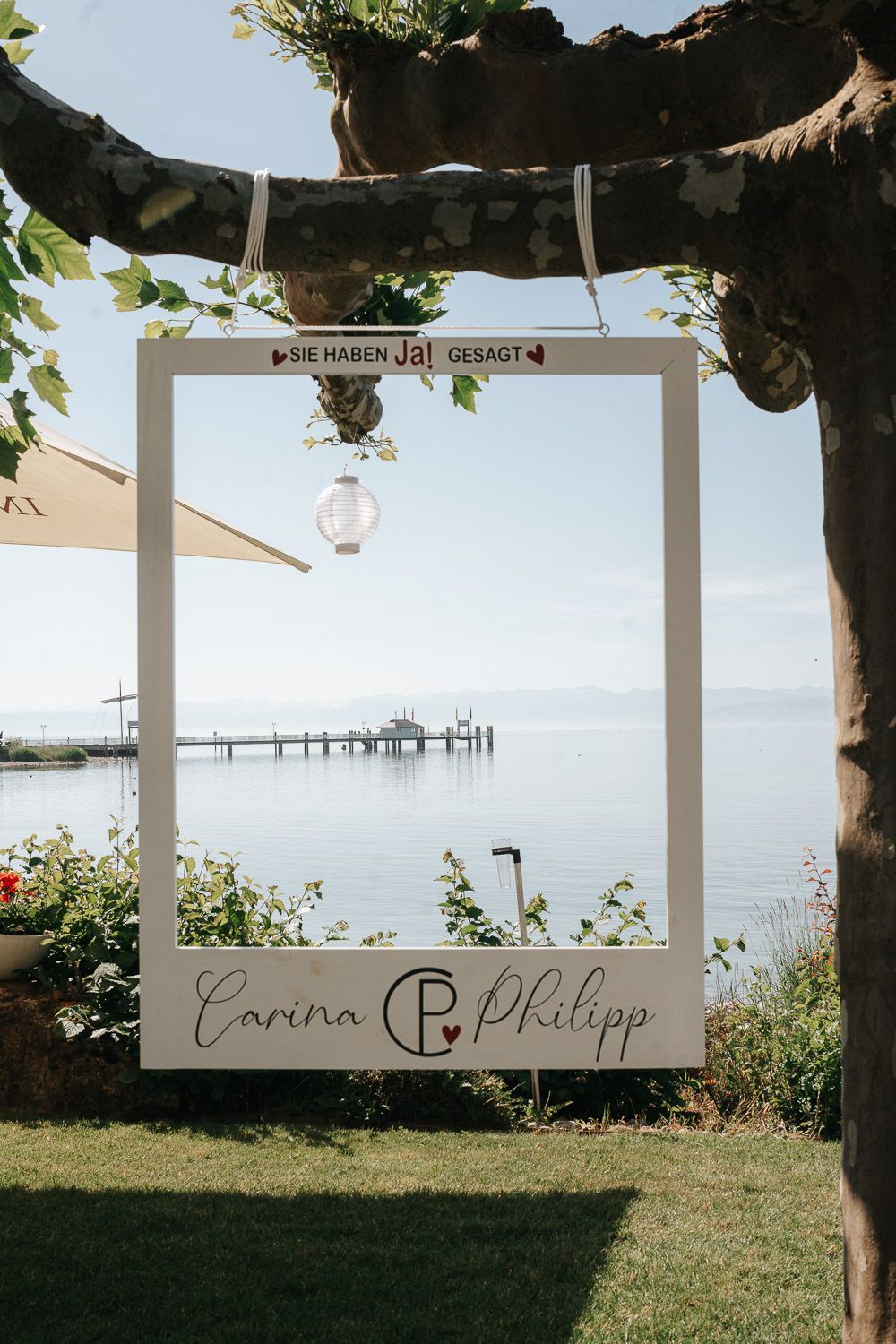 A white wedding photo frame decoration displays names overlooking a serene waterfront view.
