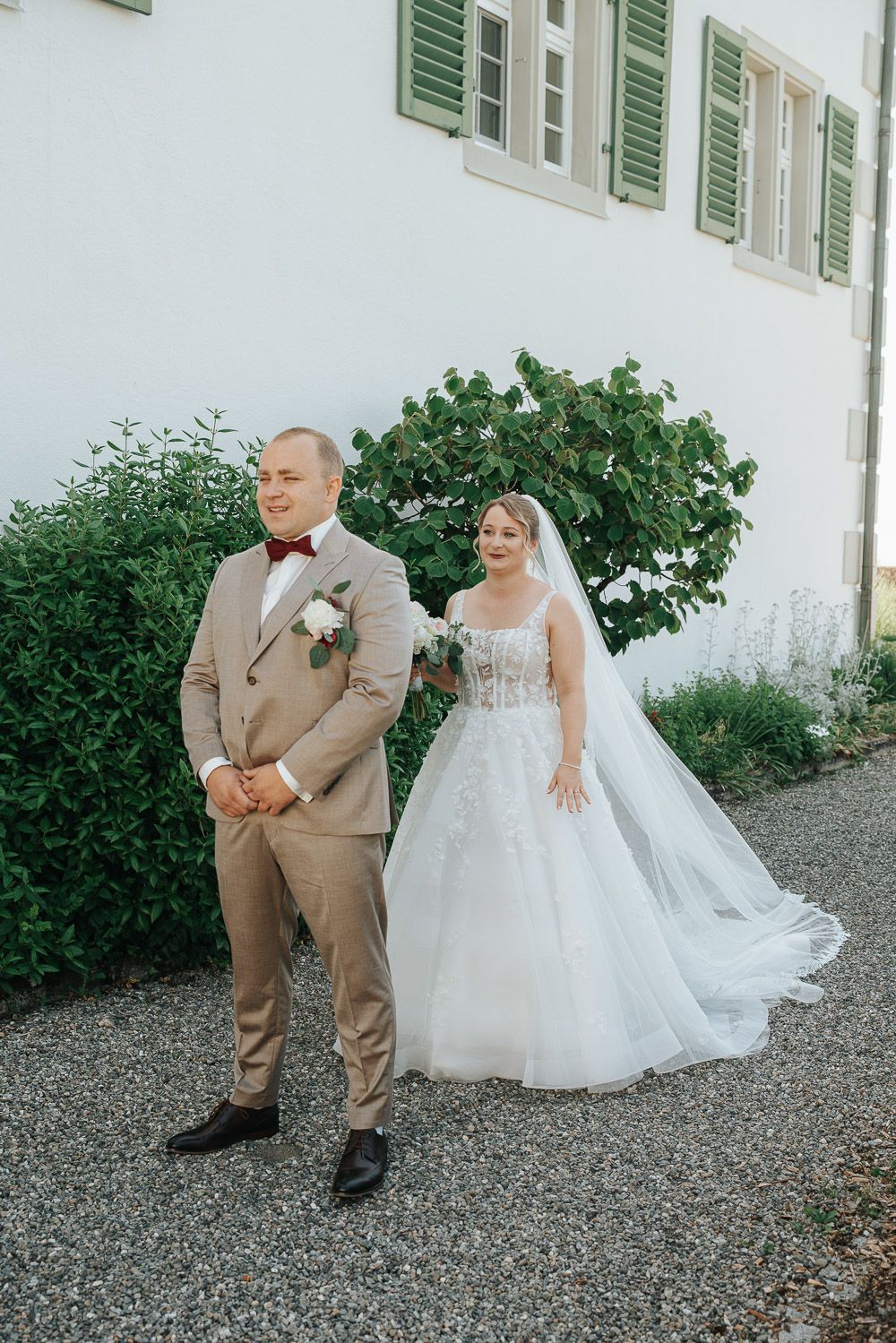 A happy couple shares a first look moment outside a white building with green shutters on their wedding day.