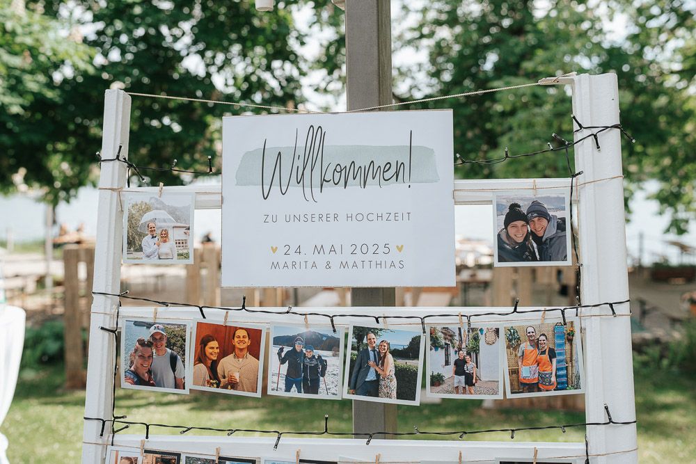 A rustic wedding welcome sign with vintage photos hanging from twine and clothespins against an outdoor garden backdrop.