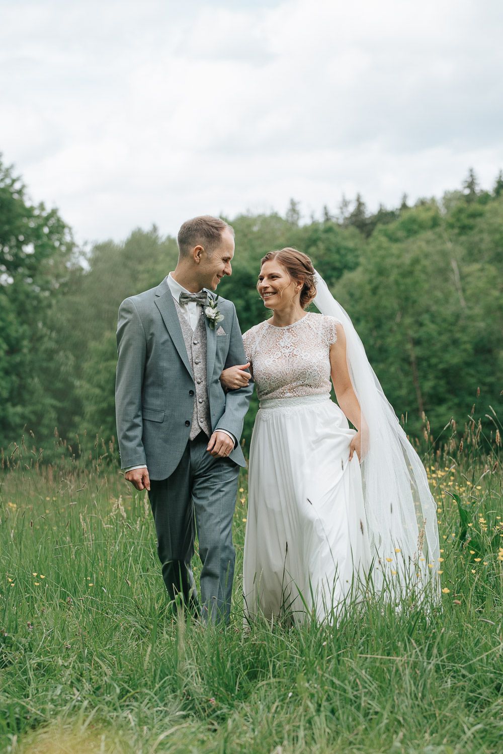 A happy couple shares a joyful moment in a meadow during their wedding, surrounded by greenery and trees.
