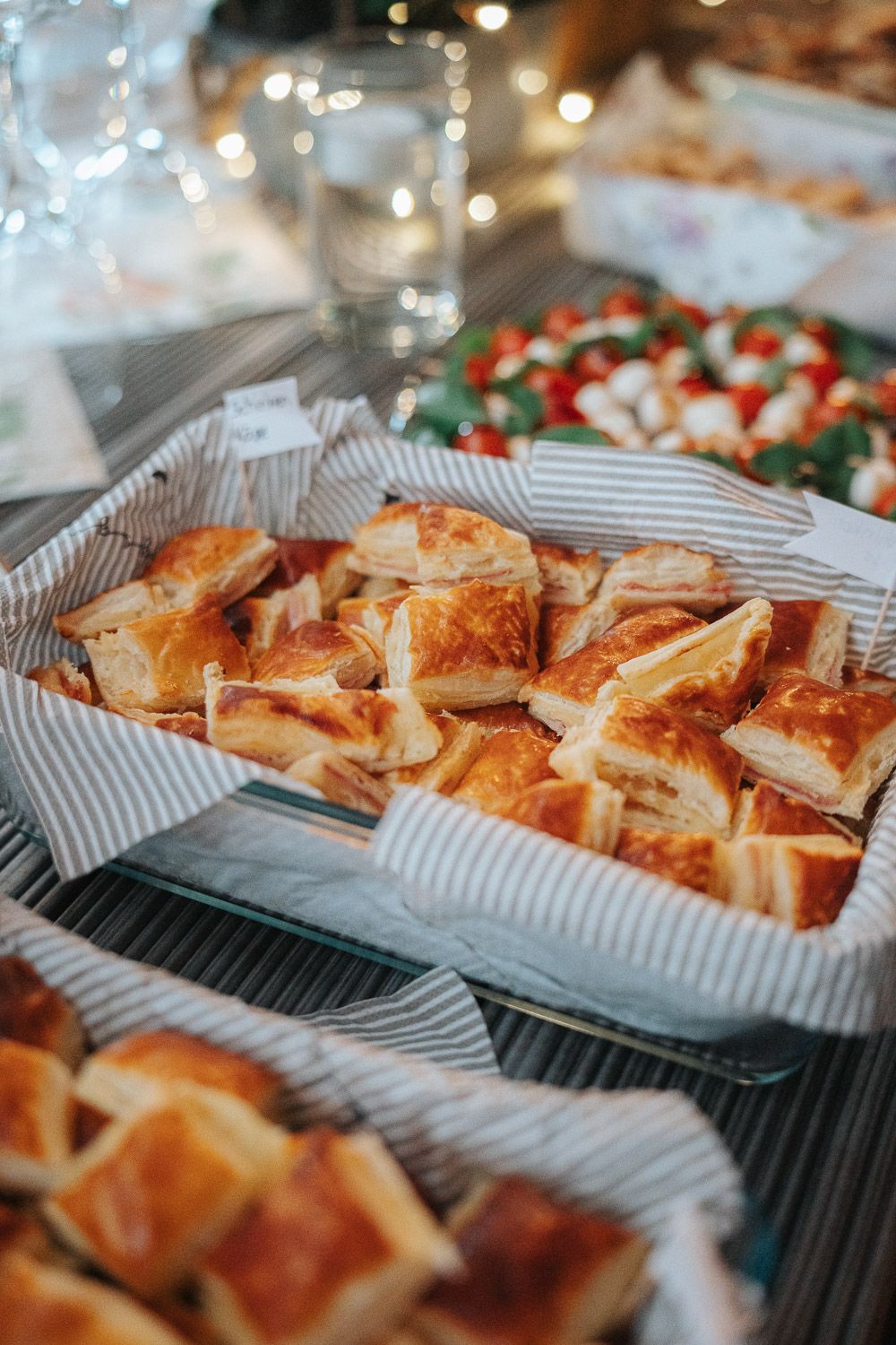 Freshly baked golden pastries arranged in black and white striped paper trays with bokeh lights in background.